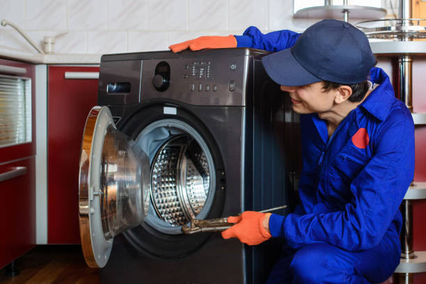 handyman in blue overalls repair/fix the washing machine in the kitchen. Young man plumber handyman in blue overalls repair/fix the washing machine in the kitchen. Washing Machine Maintenance Service stock pictures, royalty-free photos & images