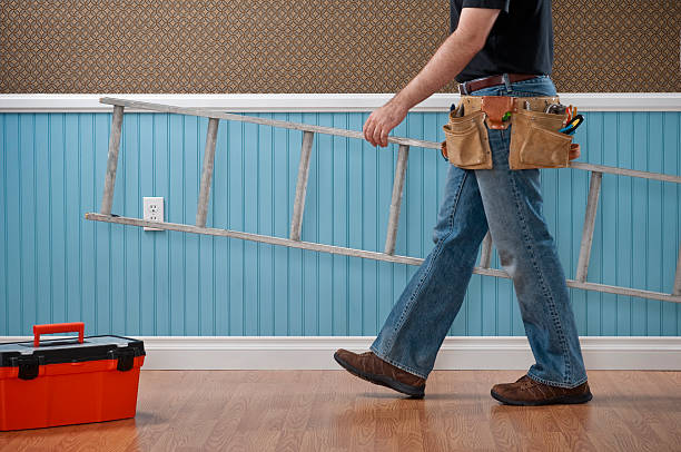 Handyman Working In Empty Room Male handyman with toolbox, tool belt and ladder  working in empty domestic room. The wall has a blue beadboard wainscoting and a patterned wallpaper. tool belt stock pictures, royalty-free photos & images