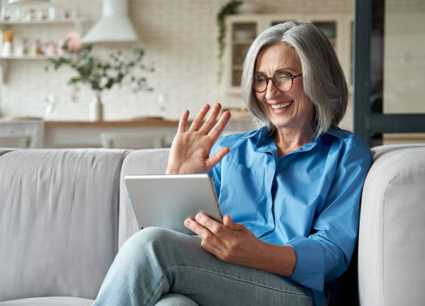 mutlu 60s yaşlı olgun orta yaşlı yetişkin kadın el sallayarak dijital tablet bilgisayar video konferans sosyal mesafe sanal aile online sohbet toplantı evde kanepede oturan tarafından arama. - video call stok fotoğraflar ve resimler