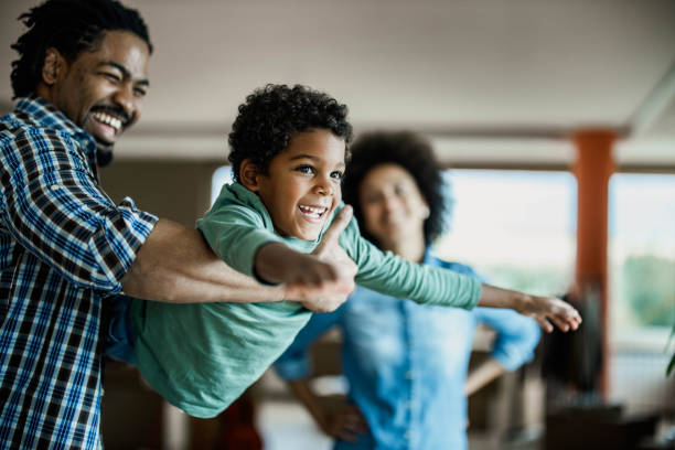 Happy African American boy having fun with his father at home. Happy black boy having fun while playing with his father at home. Woman is in the background. real people stock pictures, royalty-free photos & images