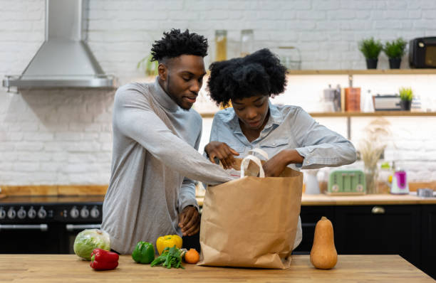 Happy African American couple at home unpacking the groceries Portrait of a happy African American couple at home unpacking the groceries from a shopping bagâ lifestyle concepts unpacking stock pictures, royalty-free photos & images