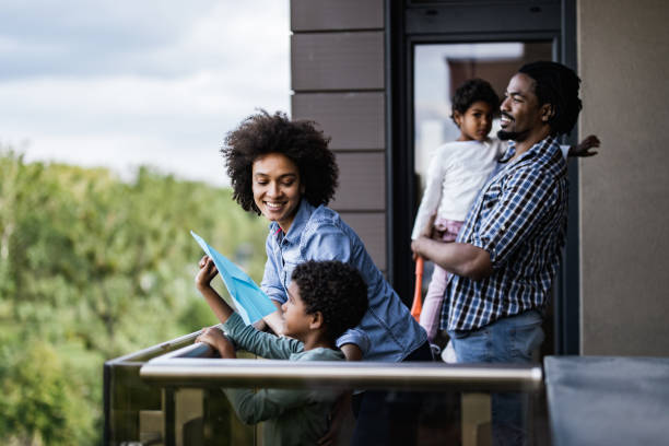 Happy African American family enjoying on a balcony. Happy black parent and their small kids enjoying on a terrace of their apartment. Focus is on woman. balcony stock pictures, royalty-free photos & images
