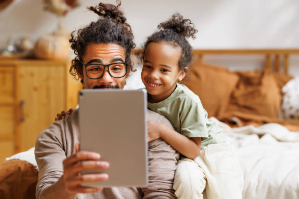 Happy african american family little son with dad watching funny videos on tablet together at home stock photo