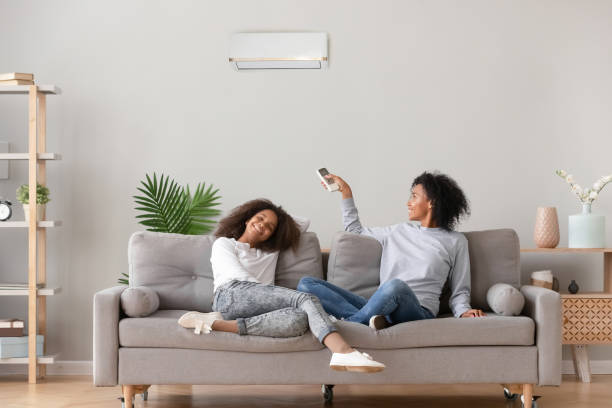 Happy african american family relaxing on sofa under air conditioner Happy african family relax on sofa under air conditioner, black mom holding remote control switch on conditioning in living room adjust comfort temperature for daughter, climate system at modern home air conditioner stock pictures, royalty-free photos & images