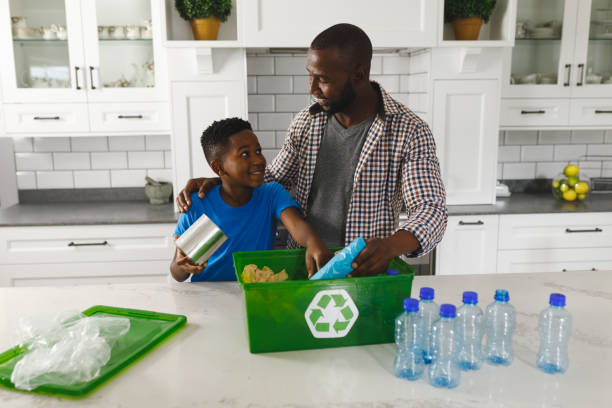 Happy african american father and son in kitchen talking and sorting rubbish for recycling stock photo