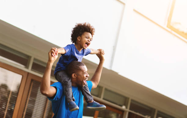 Happy African American Father carrying or piggyback his little son laughing playing outside. stock photo
