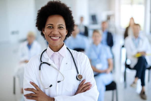 Happy African American female doctor on a healthcare seminar. Portrait of confident black doctor standing with her arms crossed while holding a seminar at convention center. female doctor stock pictures, royalty-free photos & images