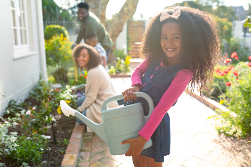 Happy african american girl and her family gardening and watering plants together. family time, having fun together at home and garden.