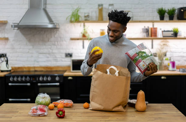 Happy African American man at home unpacking the groceries Portrait of a happy African American man at home unpacking the groceries from a shopping bag and smiling â lifestyle concepts unpacking stock pictures, royalty-free photos & images