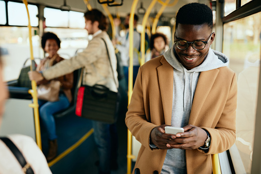 Young happy black man text messaging on smart phone while traveling by bus.