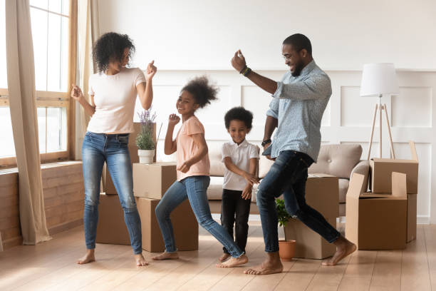 Happy african american parents and children dancing celebrating moving day Happy african american parents and cute children dancing among boxes celebrating moving day relocation renovation, active carefree funny mixed race family mom dad having fun with kids in new house child lover stock pictures, royalty-free photos & images