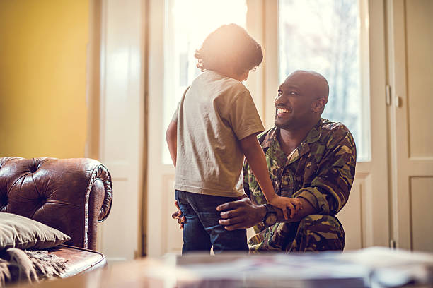 Happy African American soldier talking to his son at home. Smiling soldier reunited with his son after coming back from war. soldiers returning home stock pictures, royalty-free photos & images
