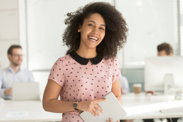 Happy african businesswoman holding digital tablet looking at camera Happy confident african american business woman employee holding digital tablet looking at camera standing in office, smiling millennial mixed race female intern manager young professional portrait trainee stock pictures, royalty-free photos & images