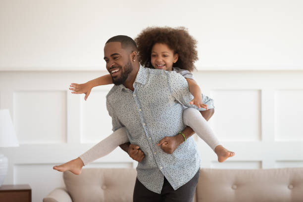 happy african dad meeliften kleine dochter met plezier thuis - piggyback funny stockfoto's en -beelden