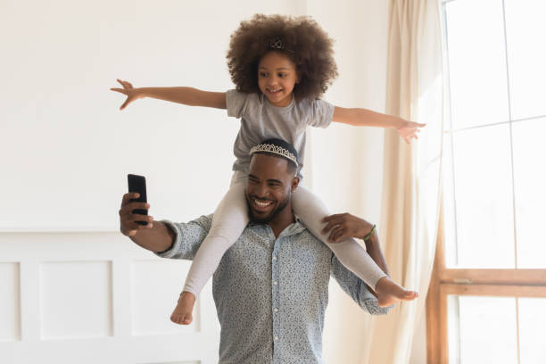 happy african dad dragen crown meeliften kleine dochter nemen selfie - piggyback funny stockfoto's en -beelden