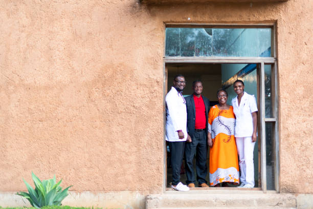Happy African doctor and nurse standing with senior couple in hospital doorway stock photo