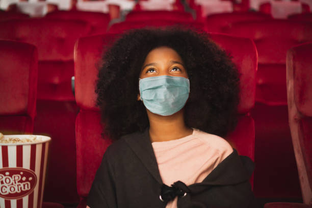 Happy african kid wearing protective face mask and watching movie in theater/theatre cinema protect infection from coronavirus covid-19, social distancing in theatre concept Happy African kid wearing protective face mask and watching movie in theater/theatre cinema protect infection from coronavirus covid-19, social distancing in theatre concept movie stock pictures, royalty-free photos & images