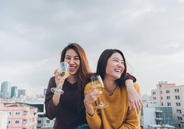 gelukkig azië vriendinnen genieten van lachen en vrolijke mousserende wijn glas op dak partij, vakantie feestelijke viering, teeage levensstijl, vrijheid en fun.lesbian paar. - sunset dining stockfoto's en -beelden