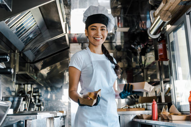glücklicher asiatischer koch hält kartonplatten in food truck - asiatischer koch stock-fotos und bilder
