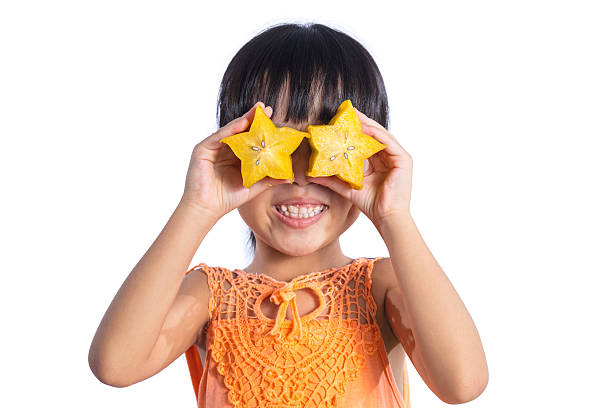 Happy Asian Chinese little girl using starfruit as glasses stock photo