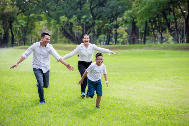 happy asian Family, parents and their children running around  in park together. father mother and son having fun and laughing outdoors . cheerful .with copy space stock photo