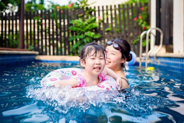 Happy asian girl with her mother having fun in the swimming pool stock photo