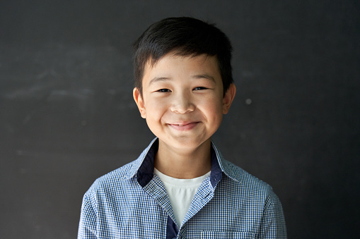 Happy cute Asian kid boy school student looking at camera at blackboard background. Smiling ethnic child pupil posing in classroom. Junior elementary education. Back to school in Asia concept Portrait