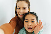 カメラに向かって手を振るかわいい女の子と幸せなアジアの母親