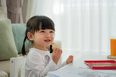 彼女は彼女の家のリビングルームに描くとき、ウエハを食べながら、大きな笑顔で幸せなアジアの幼児の女の子。