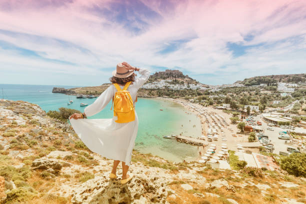 felice donna asiatica viaggia in grecia. divertirsi con la vista mozzafiato sul resort sul mare e sul centro storico di lindos sulla montagna - rodi foto e immagini stock