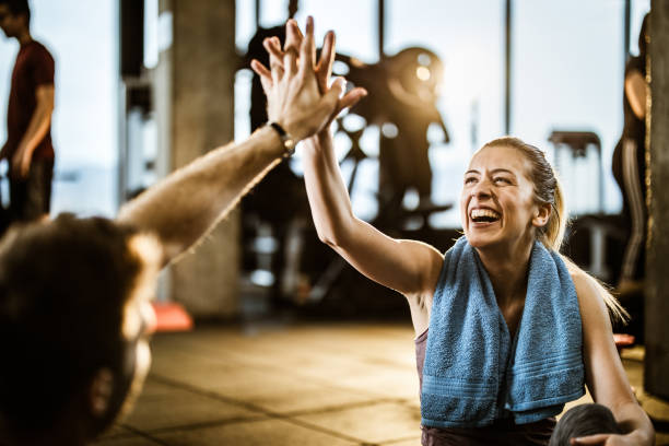glückliche athletische frau gibt high-five zu ihrem freund auf einer pause in einem fitness-studio. - trainingsraum freizeiteinrichtung stock-fotos und bilder