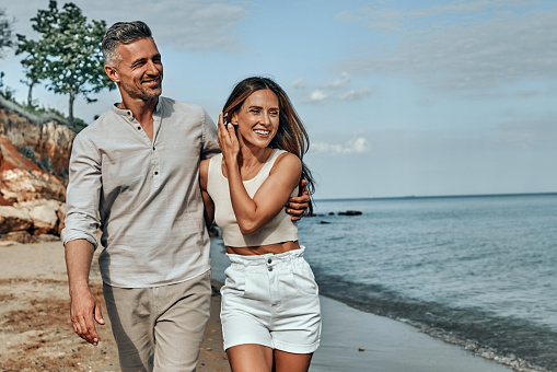 Happy attractive couple walking on beautiful sunny beach. Copy space