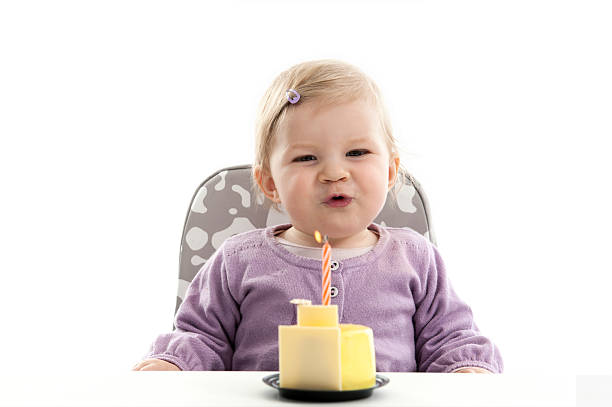happy baby blowing the candle of her first birthday cake stock photo