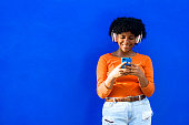 istock Happy beautiful afro american woman with orange sweater andwhite headphones listening to music on a phone, music and technology concept. 1341349186