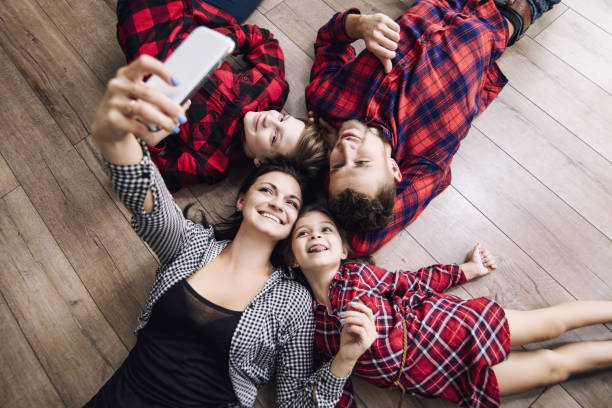 felice bella famiglia felice di fare selfie sul cellulare insieme a casa sdraiato piano vista dall'alto - floor top view foto e immagini stock