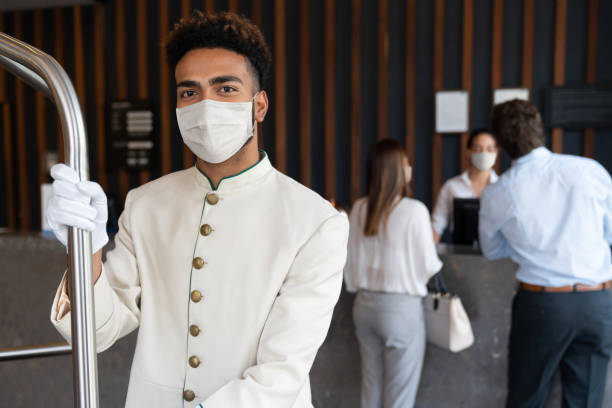 Happy bellboy working at a hotel and wearing a facemask to avoid COVID-19 Portrait of a happy bellboy working at a hotel and wearing a facemask to avoid COVID-19 - service concepts hotel stock pictures, royalty-free photos & images