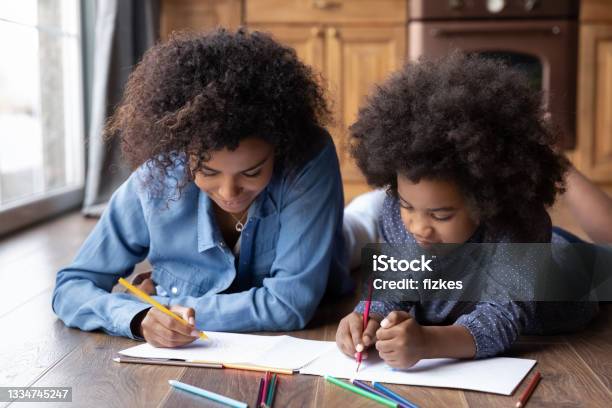 Happy biracial mom and daughter drawing in album