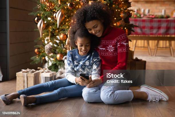 Happy biracial mom and daughter use cellphone on Christmas