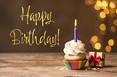 istock Happy Birthday! Delicious cupcake with candle and gift box on wooden table 1327043239