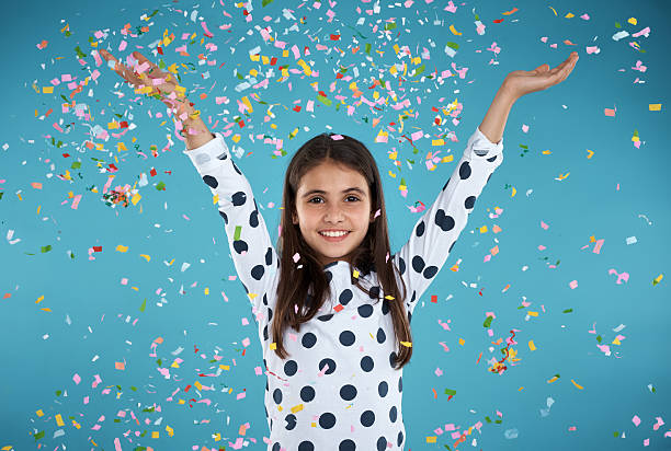 Studio portrait of a happy little girl with confetti falling all...