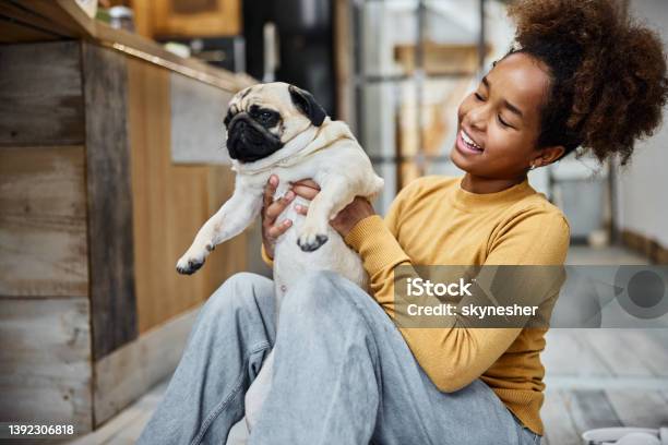 Happy black girl having fun with her pug at home.