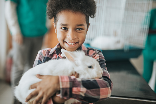 Happy African American girl with her rabbit at veterinarian's looking at camera.
