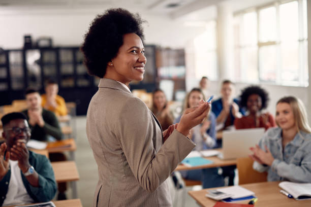 Happy black techer getting applause from her students after giving them a lecture at the university. Happy African American professor receives applause from her students while lecturing them in the classroom. professor stock pictures, royalty-free photos & images