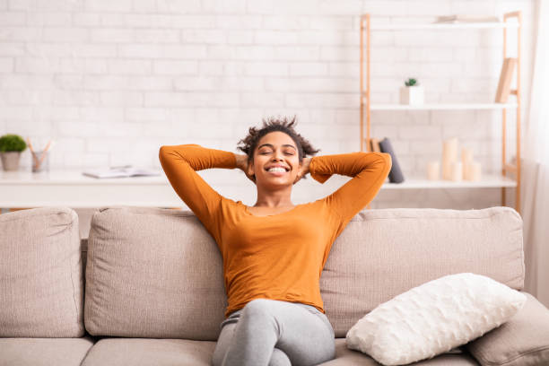 Happy Black Woman Relaxing Sitting On Sofa At Home Weekend At Home. Happy Black Woman Relaxing Sitting On Sofa Holding Hands Behind Head Enjoying Lazy Day-Off Indoor carefree stock pictures, royalty-free photos & images