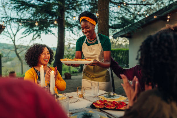 Happy black woman serving food to her family outdoors stock photo