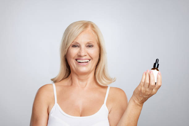A happy blond senior lady trying out new serum. Beauty photography stock photo