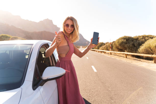 happy blonde woman showing smartphone and showing thumb up, standing near the rental car. - cargo canarias imagens e fotografias de stock