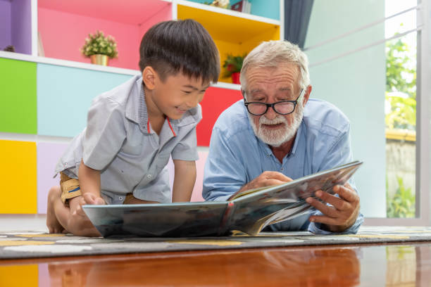 Happy boy grandson reading book with old senior man grandfather at home stock photo