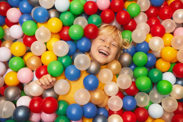 Happy boy playing with balls High angle view of happy little boy playing with colored balls indoor playground stock pictures, royalty-free photos & images