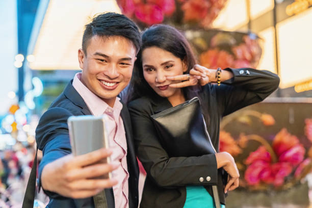 Happy Business Couple Shooting Selfies Kuala Lumpur Asian businessman and businesswoman having fun together, joking at night shooting selfies with their mobile phone after arriving from a business trip in downtown Kuala Lumpur. Pavilion KL, Bukit Bintang, Kuala Lumpur, Malaysia, Asia bukit bintang stock pictures, royalty-free photos & images